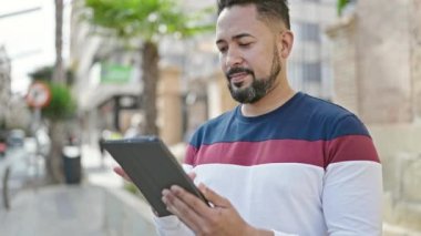 Young latin man smiling confident using touchpad at street