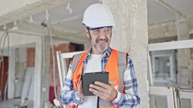 Orta yaşlı inşaatçı inşaat alanında dokunmatik ped kullanarak gülümsüyor.