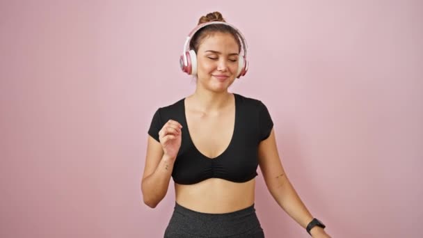 穿着运动服的年轻漂亮的惊慌失措的女人 在孤零零的粉色背景下听着音乐跳舞 — 图库视频影像