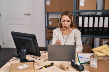 Küçük bir iş yerinde çalışan İspanyol bir kadın. Kulaklık takıyor, kamerayı işaret ediyor. Kendine güvenen bir jest, ciddi görünüyor. 