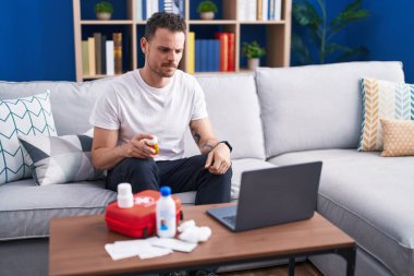 Genç İspanyol adam dizüstü bilgisayarda ilk yardım çantasının nasıl kullanılacağını seyrediyor. Düşünme tavrı ve ayık yüz ifadesi. Kendine güveni tam görünüyor. 