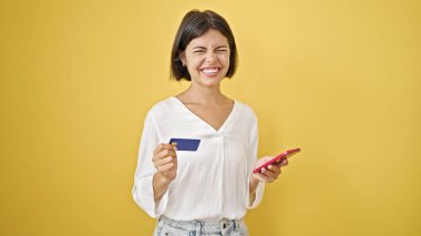 Akıllı telefon ve kredi kartıyla alışveriş yapan genç, güzel İspanyol kadın izole edilmiş sarı arka planda