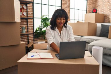 Genç, güzel, Latin bir kadın yeni evinde dizüstü bilgisayar kullanıyor.