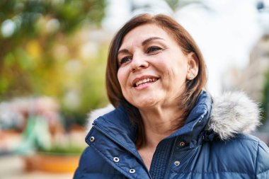 Orta yaşlı bir kadın parkta kendinden emin bir şekilde gülümsüyor.
