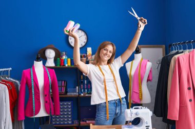 Young blonde girl tailor smiling confident holding scissors and thread at sewing studio