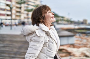 Orta yaşlı kadın deniz kenarında gözleri kapalı nefes alıyor.