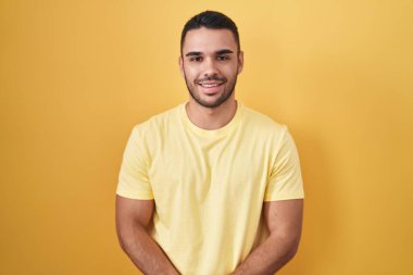 Sarı arka planda duran genç İspanyol adam ellerini kavuşturup gülümseyerek gevşemiş ve neşeliydi. Başarı ve iyimserlik 