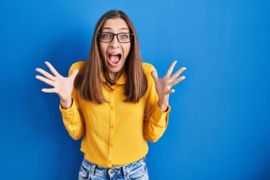 Mavi arka planda duran gözlüklü genç bir kadın çılgın ve başarıyı kollarını kaldırıp heyecanla haykırarak kutluyor. Kazanan konsept 