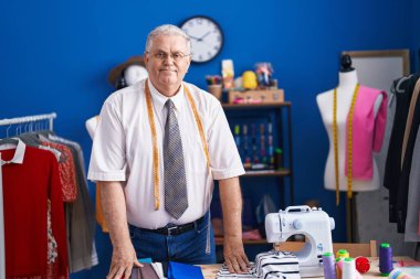 Orta yaşlı, gri saçlı, terzi dükkanında kendine güvenen bir terzi.