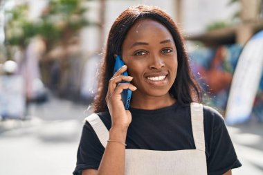 Genç Afrikalı Amerikalı kadın gülümsüyor. Kendine güveni tam. Sokakta akıllı telefondan konuşuyor.