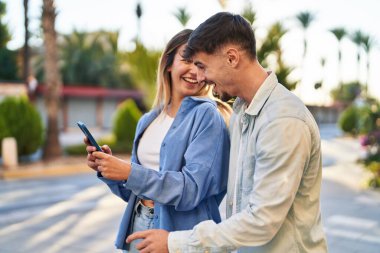Genç adam ve kadın çift sokakta akıllı telefon kullanarak gülümsüyor.