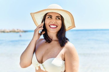 Young beautiful hispanic woman tourist smiling confident talking on smartphone at seaside