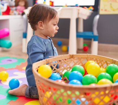 Anaokulunda yerde oturmuş toplarla oynayan sevimli İspanyol çocuk.