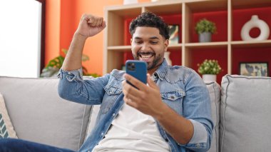 Afro-Amerikalı adam evinde akıllı telefon kullanıyor.