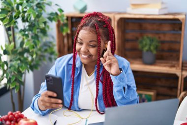 Saçları örgülü, akıllı telefon kullanan, bir fikir veya soruyla gülümseyen, mutlu yüzlü Afro-Amerikalı bir kadın. 