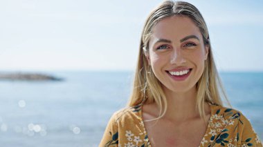 Young blonde woman smiling confident standing at seaside