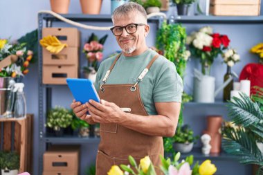 Çiçekçide dokunmatik ped kullanarak gülümseyen gri saçlı bir çiçekçi.