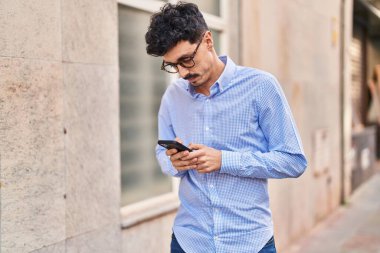 Beyaz bir adam sokakta ciddi bir ifadeyle akıllı telefon kullanıyor.