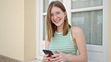 Sokakta akıllı telefon kullanan, kendine güvenen genç sarışın kadın.