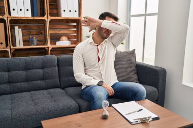 Danışma ofisinde sakallı, genç, İspanyol bir adam. Gözleri kollarıyla kapatıyor, ciddi ve üzgün görünüyor. Görme, saklama ve reddetme konsepti 