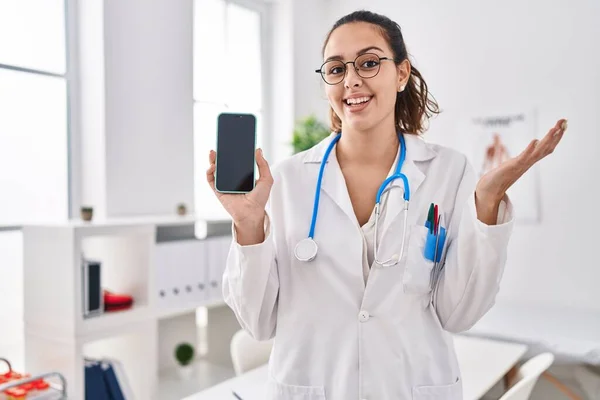Joven Doctora Hispana Sosteniendo Smartphone Mostrando Pantalla Gritando Orgullosa Celebrando —  Fotos de Stock