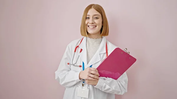 年轻的金发女医生微笑着 自信地拿着剪贴板遮住孤立的粉色背景 — 图库照片
