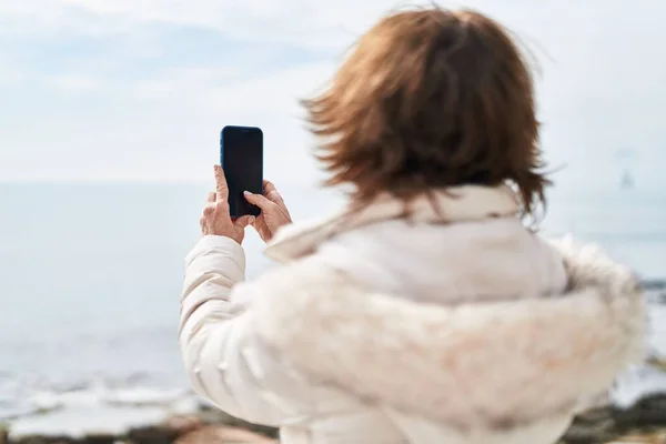 中世の女性は海辺でスマートフォンで写真を撮る — ストック写真