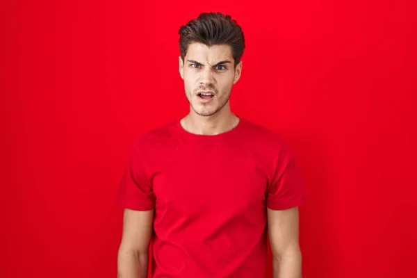 Mladý Hispánec Stojí Nad Červeným Pozadím Šokované Tváři Vypadá Skepticky — Stock fotografie