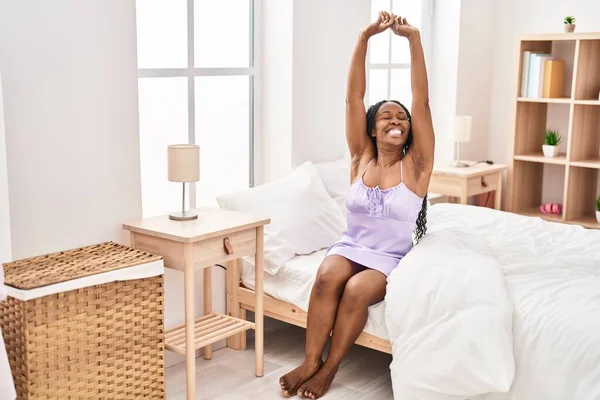 stock image African american woman stretching arms sitting on bed at bedroom