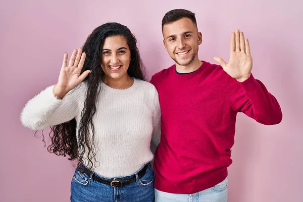 Young Hispanic Couple Standing Pink Background Waiving Saying Hello Happy — Zdjęcie stockowe