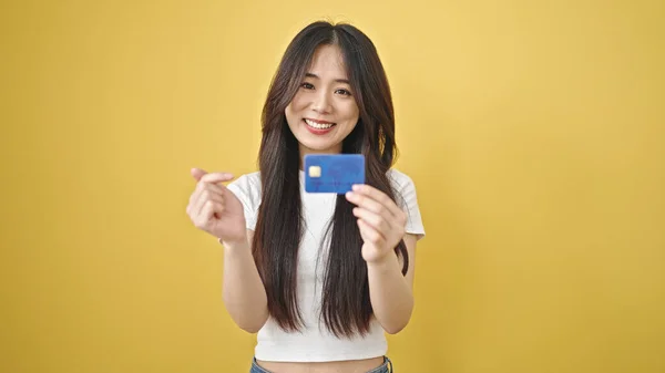 Young chinese woman smiling confident pointing to credit card over isolated yellow background
