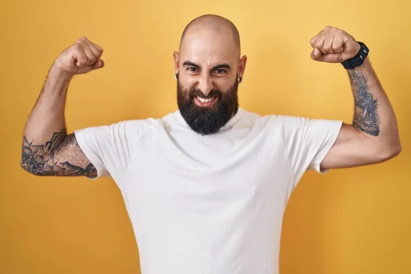 Jovem Hispânico Com Barba Tatuagens Sobre Fundo Amarelo Mostrando Músculos — Fotografia de Stock