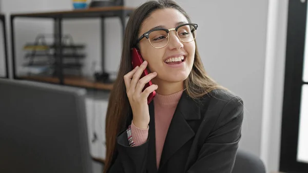 若い美しいヒスパニック系の女性のビジネスワーカーがオフィスで働くスマートフォンで話しています — ストック写真