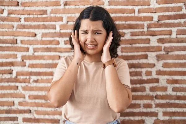 年轻的惊慌失措的女人站在砖墙上 用手指捂住耳朵 恼怒地看着嘈杂的音乐 聋人概念 — 图库照片