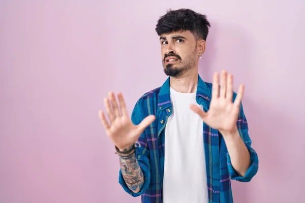 ピンクの背景の上に立っているひげを持つ若いヒスパニック系の男は恐れていると手で恐怖表現のジェスチャーを停止し ショックで叫んでいる パニックの概念 — ストック写真