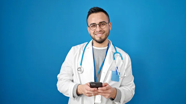 Homme Hispanique Médecin Souriant Confiant Utilisant Smartphone Sur Fond Bleu — Photo