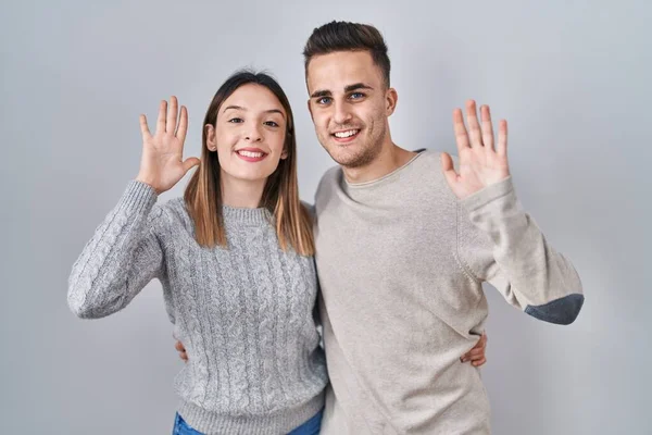 Young Hispanic Couple Standing White Background Waiving Saying Hello Happy — Stockfoto