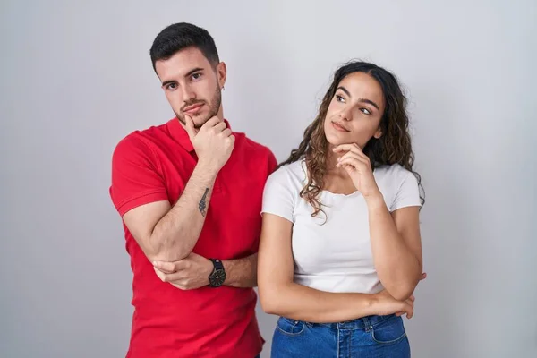Young Hispanic Couple Standing Isolated Background Hand Chin Thinking Question — Stock Photo, Image
