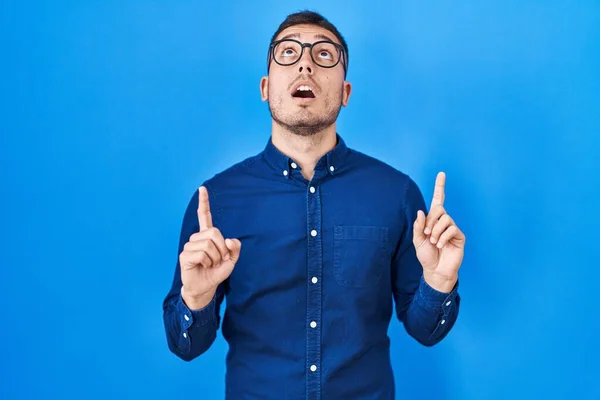 Jovem Hispânico Vestindo Óculos Sobre Fundo Azul Espantado Surpreso Olhando — Fotografia de Stock
