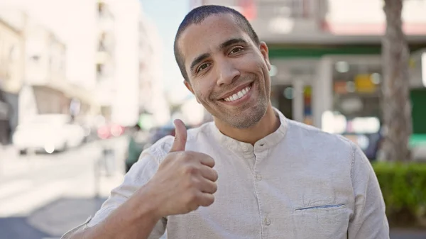 Joven Hombre Hispano Sonriendo Confiado Haciendo Signo Con Pulgar Calle —  Fotos de Stock