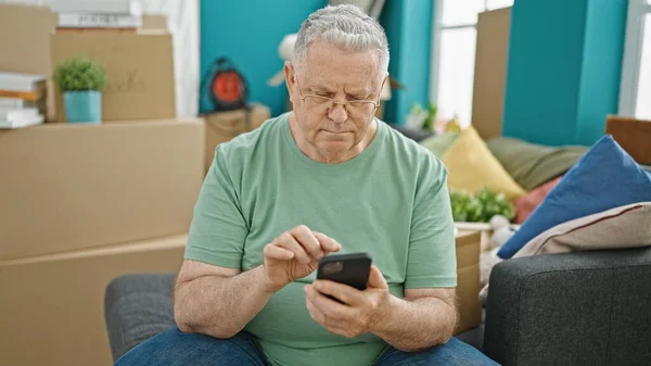 中年白髪男使用スマートフォン座って上のソファに新しい家 — ストック写真