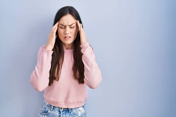ストレスが原因で頭の痛みのために頭の上に手で青の背景に立って若いブルネットの女性 片頭痛 — ストック写真
