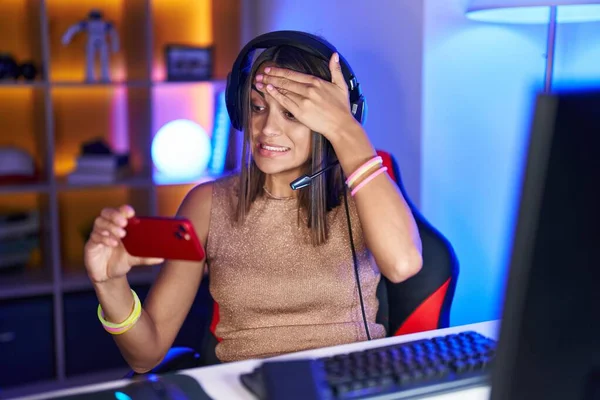 stock image Young hispanic woman playing video games with smartphone stressed and frustrated with hand on head, surprised and angry face 