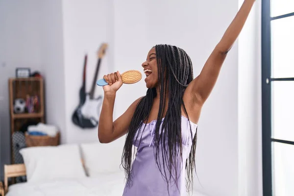 stock image African american woman singing song using brush as a microphone at bedroom