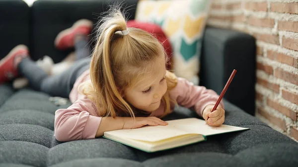 愛らしいブロンド女の子就学前学生嘘上のソファ描画上のノートブックで自宅 — ストック写真