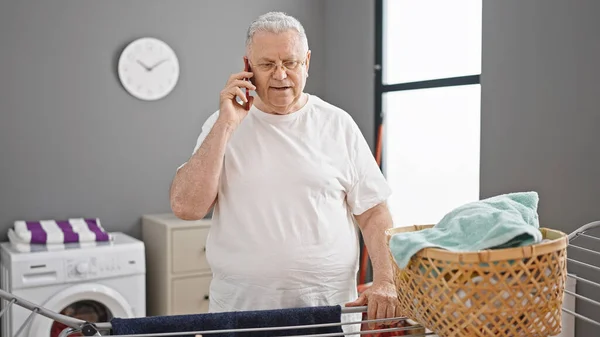中年白发男人在洗衣房用智能手机聊天 把衣服挂在晾衣绳上 — 图库照片