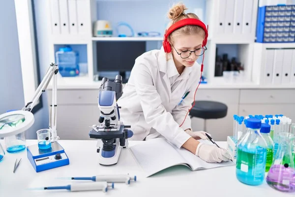 Young Blonde Woman Scientist Listening Music Writing Notebook Laboratory — Stock Photo, Image