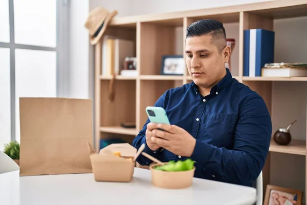 Jovem Hispânico Comendo Tirar Comida Usando Smartphone Relaxado Com Expressão — Fotografia de Stock