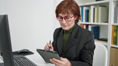 Yetişkin İspanyol kadın öğretmen kütüphane üniversitesindeki dokunmatik sayfaya not alıyor.