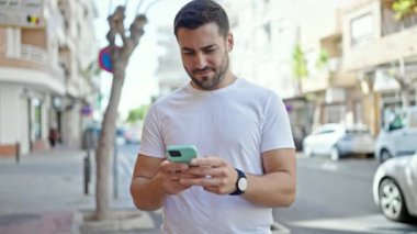 Genç İspanyol adam akıllı telefon kullanıyor. Sokakta kazanan yüz ifadesi var.